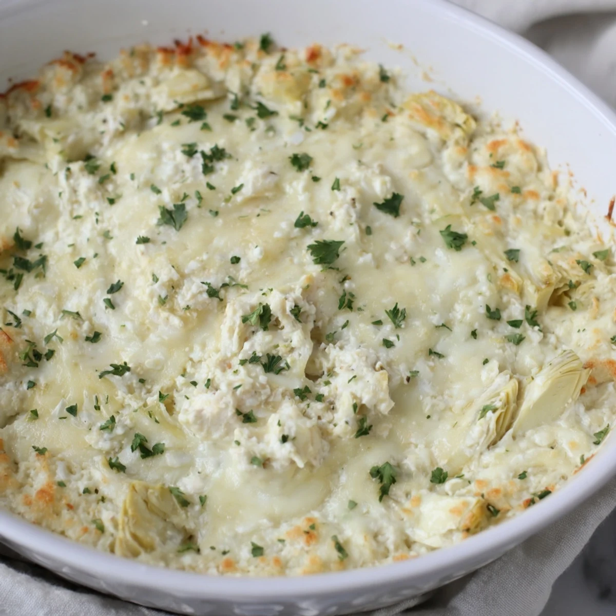 Golden-brown baked artichoke dip, featuring melted mozzarella, served with crisp crackers.