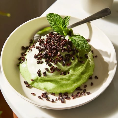 Vibrant Grinch Green Mint Matcha Chia Pudding, topped with cacao nibs and fresh mint, awaits in a bowl.