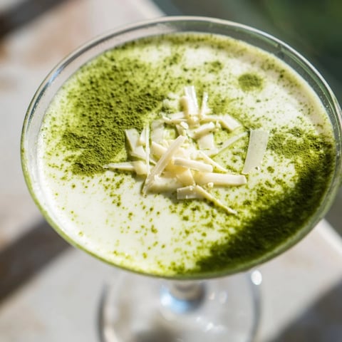 A chilled Matcha Martini cocktail rests on a marble surface, garnished with a dusting of vibrant green matcha powder.