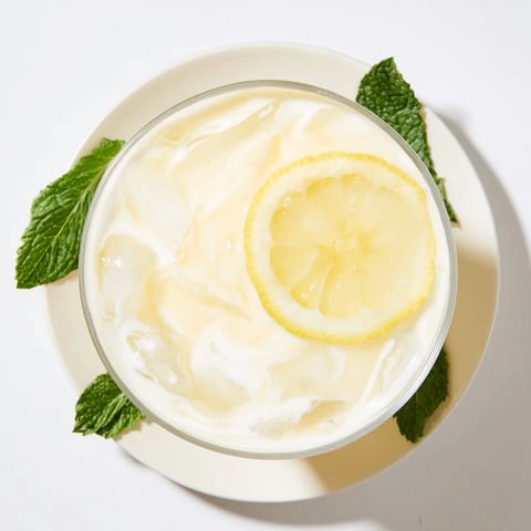 Creamy lemonade drink in a tall glass with ice, lemon slices, and mint leaves.  