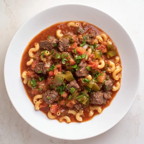 This close-up shows rustic goulash with tender beef, colorful veggies, and perfectly cooked pasta.