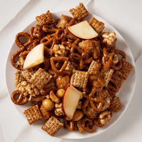 A close-up of holiday-ready Party Mix showcasing the crispy cereal, pretzels, and apple pieces.