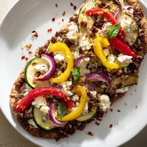 Warm naan bread pizza, topped with olives, feta, and colorful roasted vegetables.