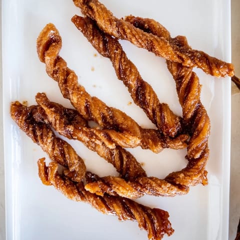 Twisted strips of Spiced Bacon Twists baked until crisp, served on a white plate with a drizzle of maple syrup.