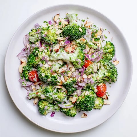 Bright green broccoli florets tossed in a creamy garlic Parmesan dressing with red onion and cherry tomatoes in a white bowl.