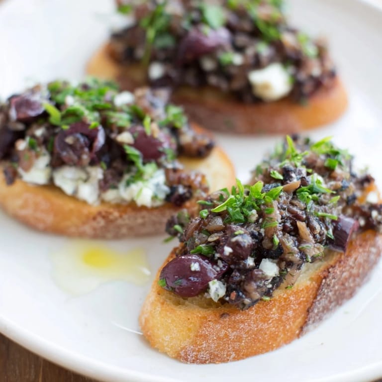 Close-up of a bowl of black olive tapenade served alongside toasted, golden crostini.