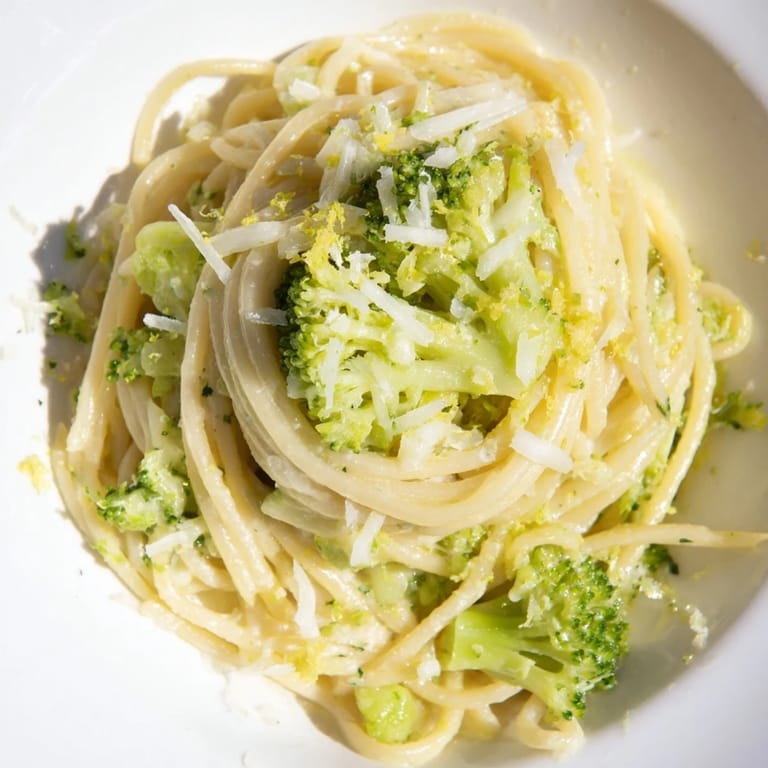 Close-up of One-Pot Lemon Broccoli Pasta garnished with fresh basil and grated Parmesan on a rustic table.  