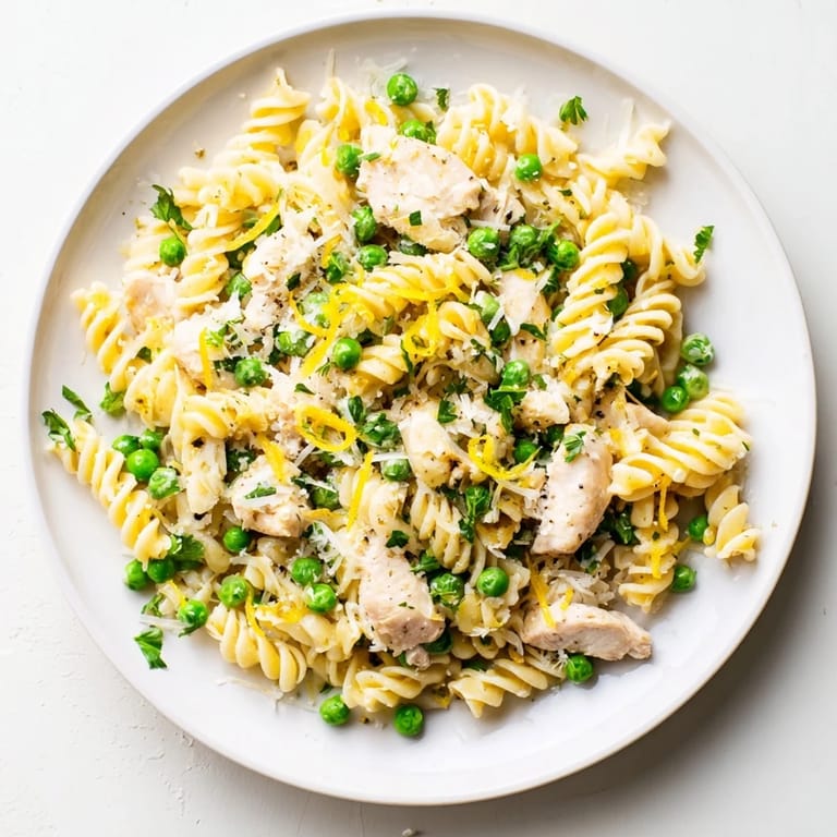 Family-friendly Garlic Butter Chicken & Pea Pasta features golden chicken, vibrant green peas, and curly pasta coated in buttery sauce.