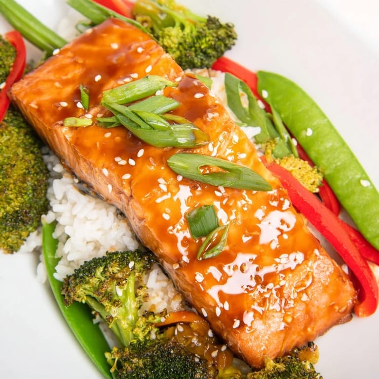 A close-up of glazed Maple Soy Glazed Salmon atop jasmine rice with crisp broccoli and snap peas.
