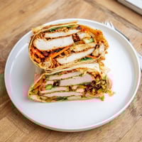 Freshly assembled Honey Chili Crunch Chicken Wrap with juicy chicken, shredded lettuce, and vibrant carrots in a warm flour tortilla.