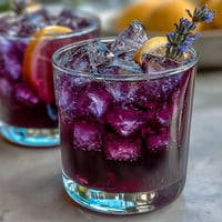 Vibrant Purple Rain Lavender Lemonade Refresher garnishes glasses with citrus and ice.